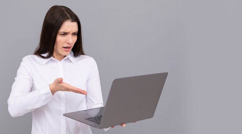 Kobieta trzyma otwartego laptopa i z oburzoną miną pokazuje na ekran
