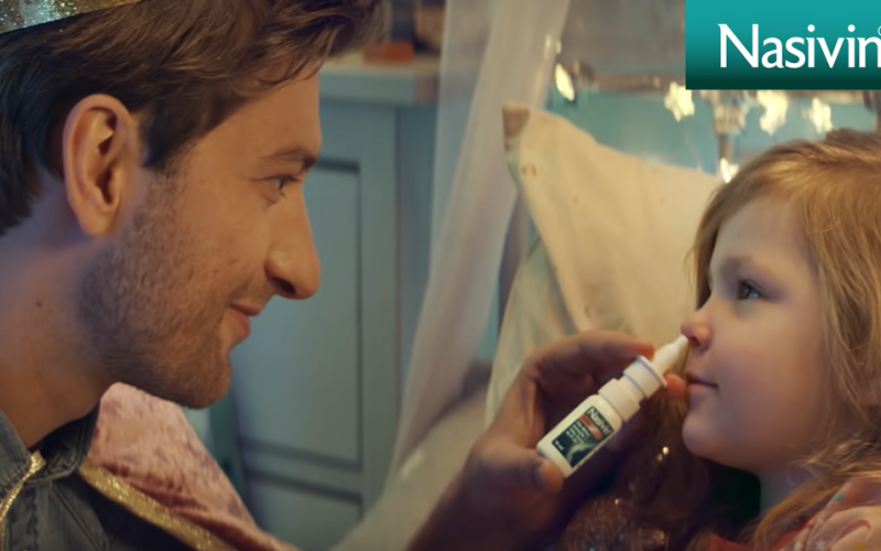 Uśmiechnięty mężczyzna aplikuje małej dziewczynce spray do nosa
